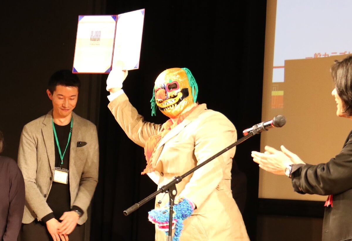 表彰式でピエロ仮面を被っているプロレスラー受賞者の写真